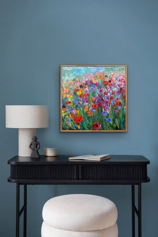 Decorative setup with a black console table, lamp, and ottoman against a blue wall with a floral painting.
