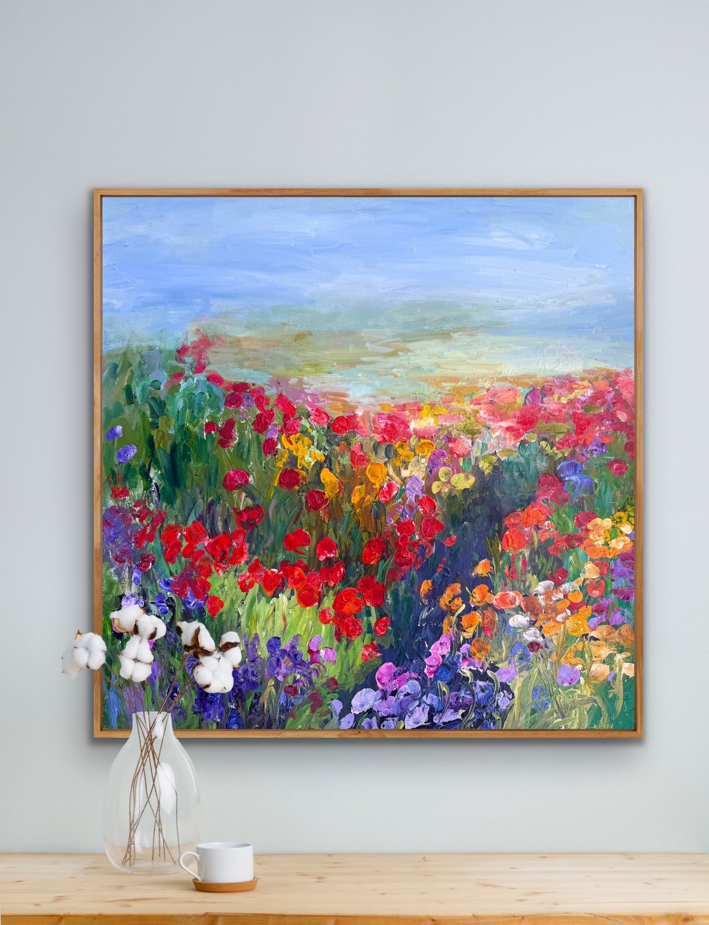 Framed impressionist landscape painting by Maria-Victoria Checa shown above a shelf with white flowers.