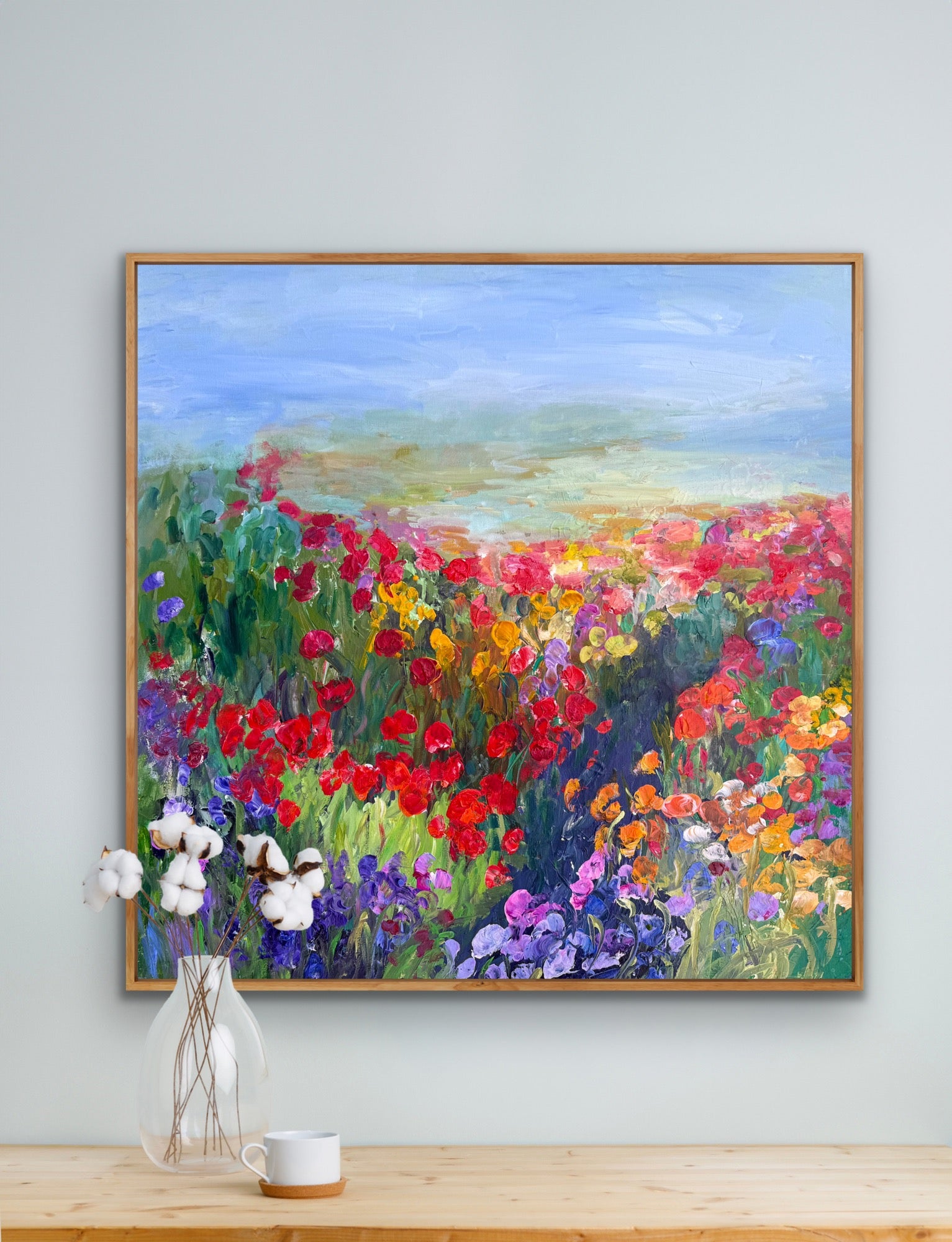 Framed impressionist landscape painting by Maria-Victoria Checa shown above a shelf with white flowers.