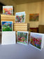 five impressionist flower field greeting cards displayed around a wood box with white envelopes, by Washington DC artist Maria-Victoria Checa