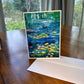 Green water lily pond greeting card with yellow and pink lily pads and lush tree reflections — impressionist art card by Maria-Victoria Checa