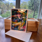 Abstract art greeting card in clear sleeve leaning against natural wood gift box showing red, blue and green painterly detail — Checa Art card set