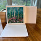 Checa Art square greeting card open showing blank white interior next to birch forest card and natural wood gift box