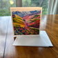Mountain valley greeting card with vibrant wildflowers in pink, red, orange and purple cascading toward snowy peaks — square impressionist art card by Maria-Victoria Checa