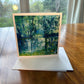 Forest pond greeting card with luminous teal tree reflections shimmering on still blue-green water — square impressionist art card by Maria-Victoria Checa
