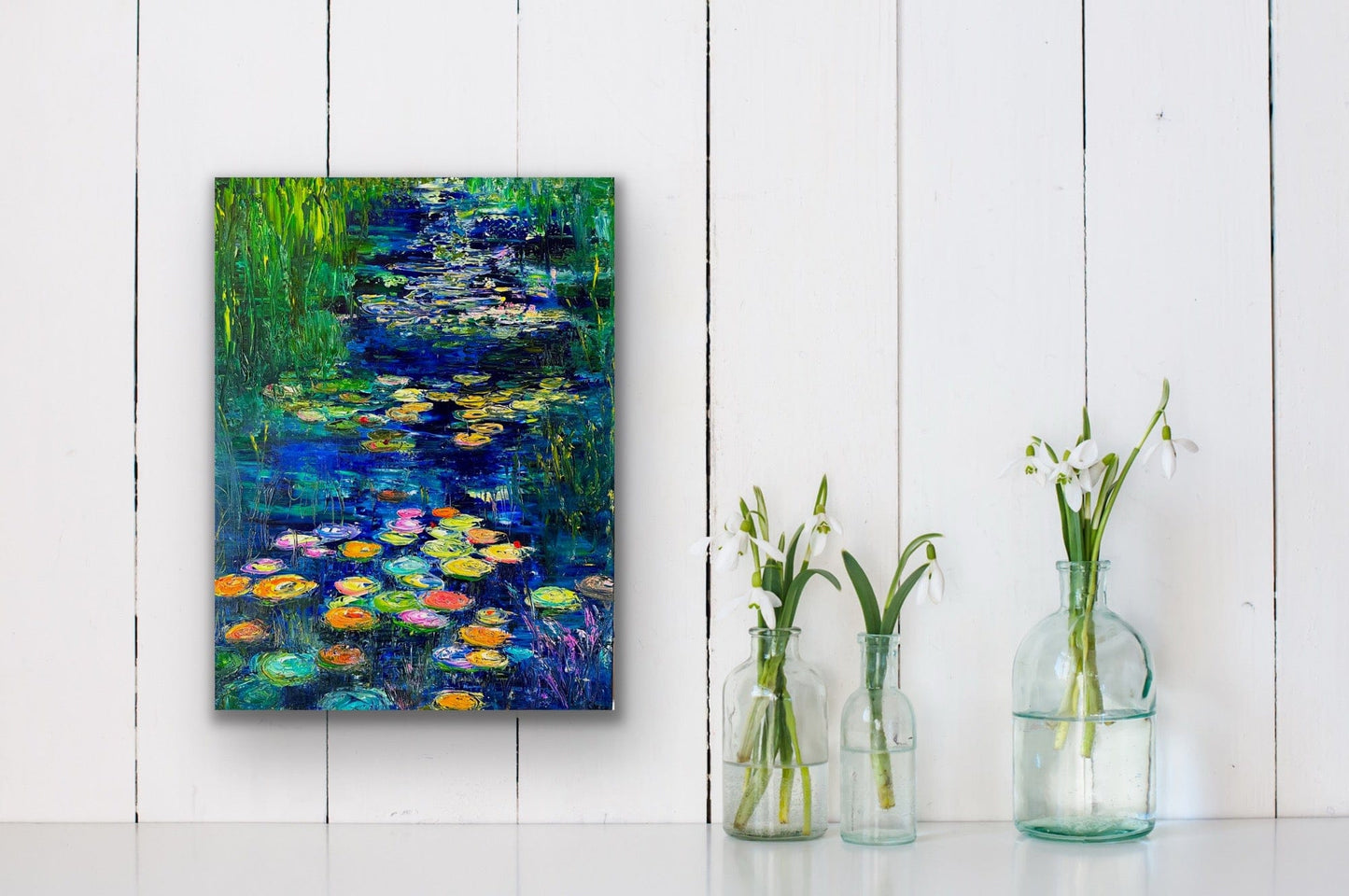 Blue Lily River art print displayed on white wall above glass vases with flowers