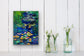 Blue Lily River art print displayed on white wall above glass vases with flowers