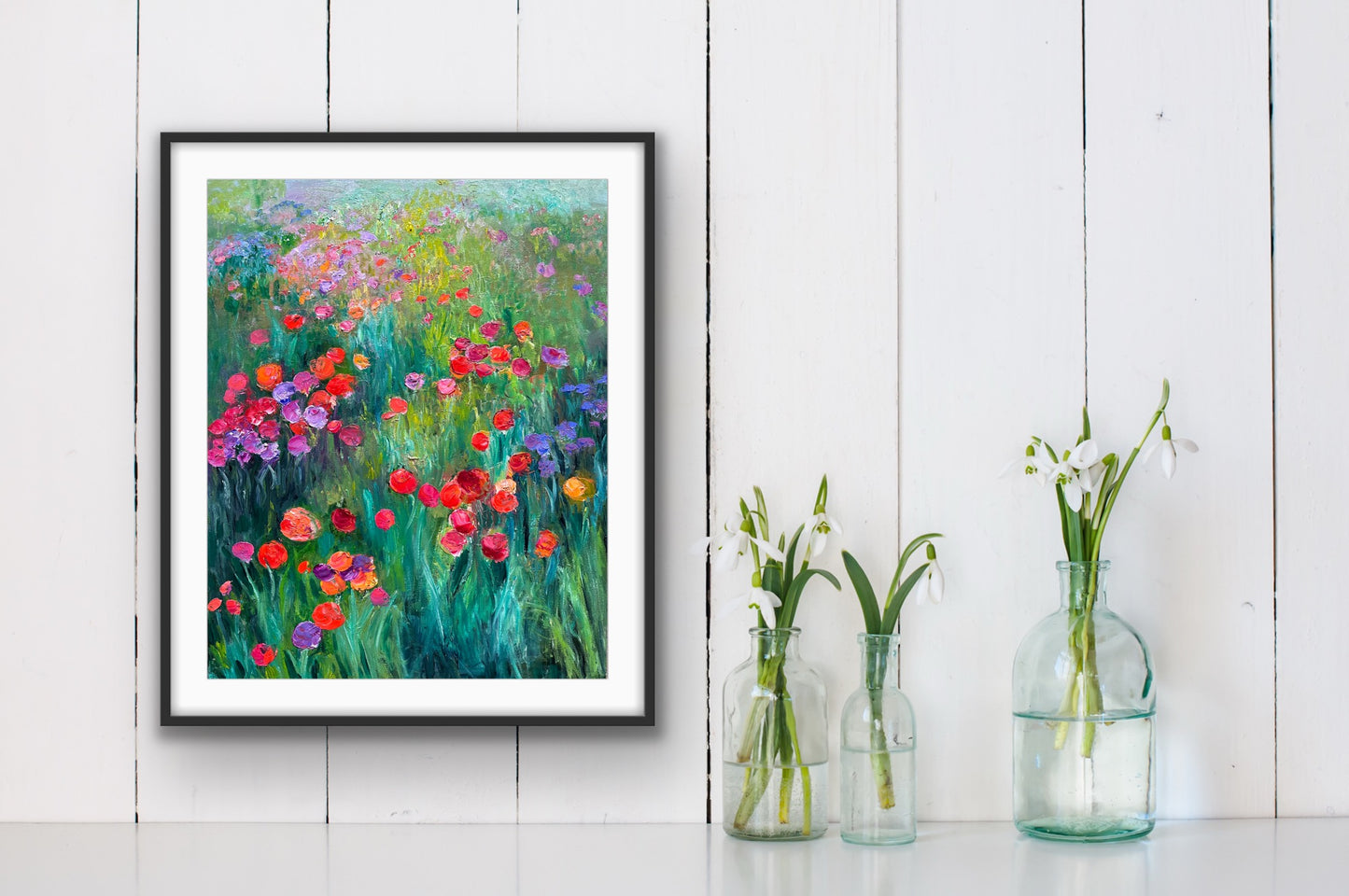 Framed paper print of “Fantasia” by Maria-Victoria Checa displayed on a white wall above glass vases with fresh flowers.