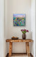 Framed fine art print of ‘Flower Field at Dusk’ by Maria-Victoria Checa displayed in a hallway above a wooden console with a vase of tulips.
