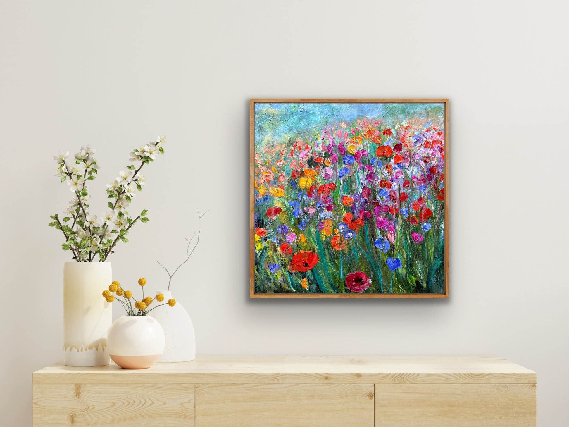 Framed painting of a colorful floral scene on a wall above a wooden cabinet with decorative vases.