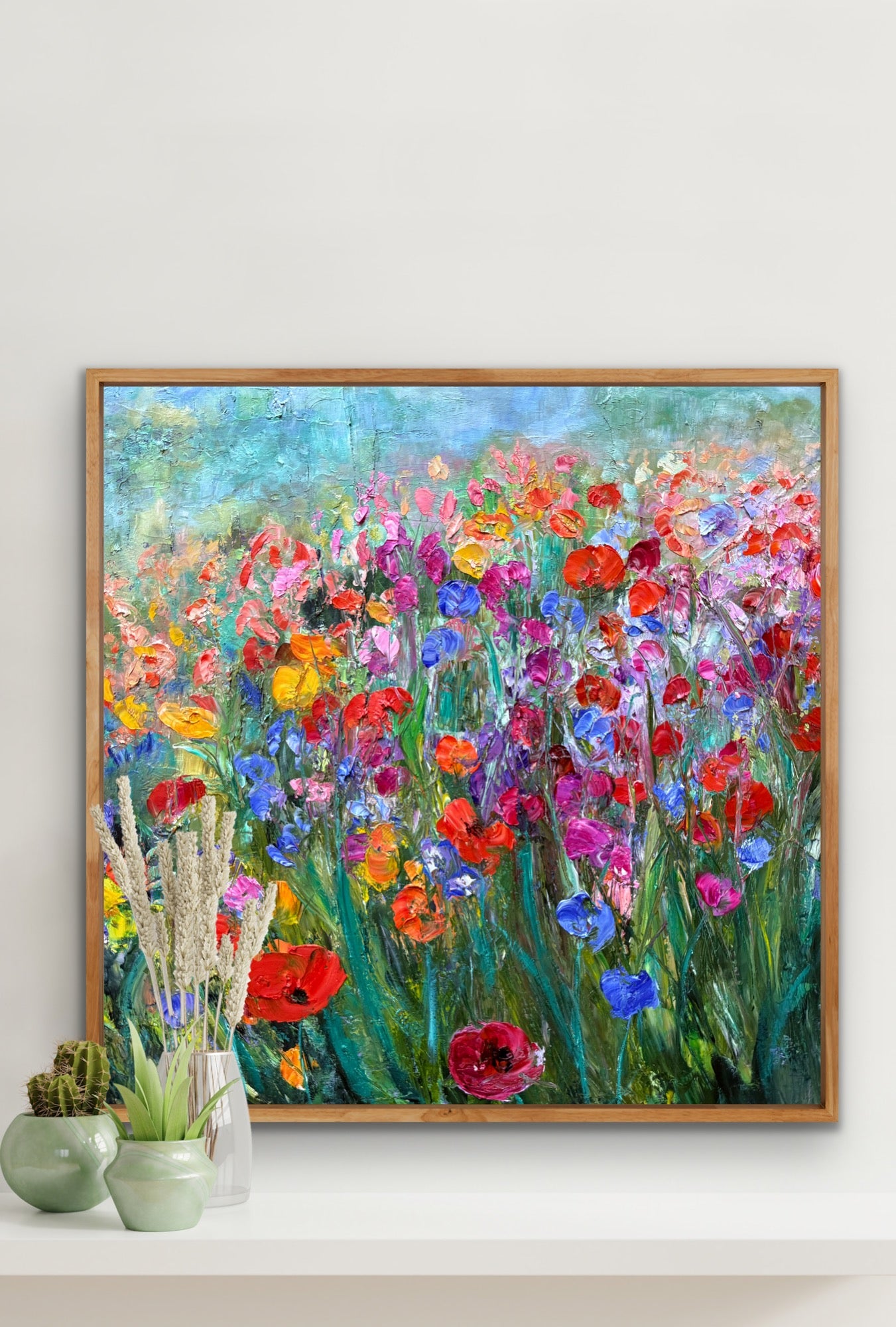Framed painting of a colorful floral landscape on a white wall.
