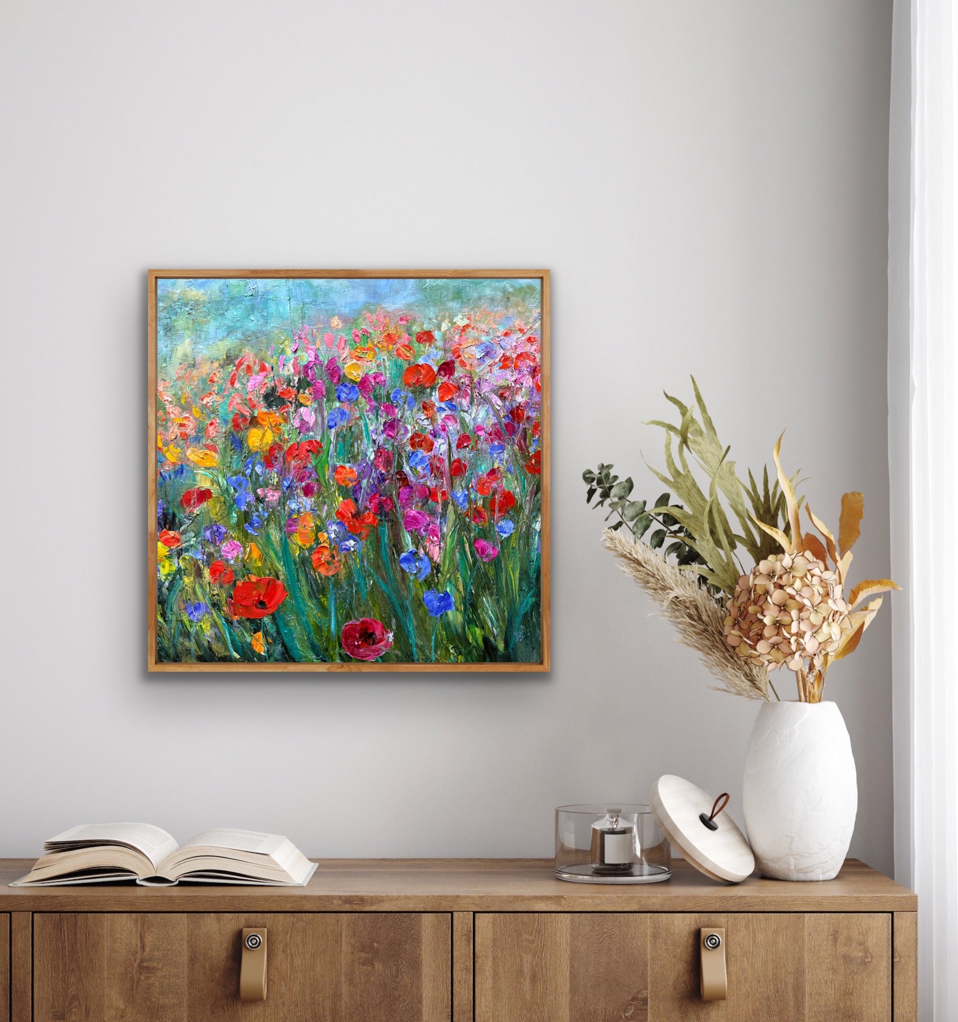Framed floral painting on a wall above a wooden cabinet with decorative items.