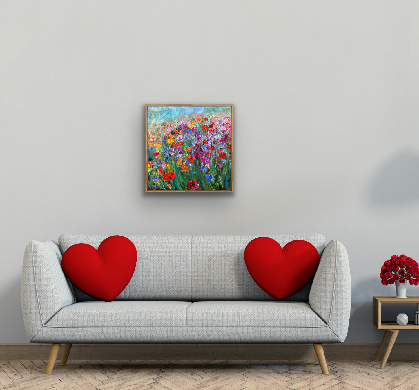 Gray sofa with red heart-shaped cushions, colorful floral painting on the wall, and small table with red flowers.
