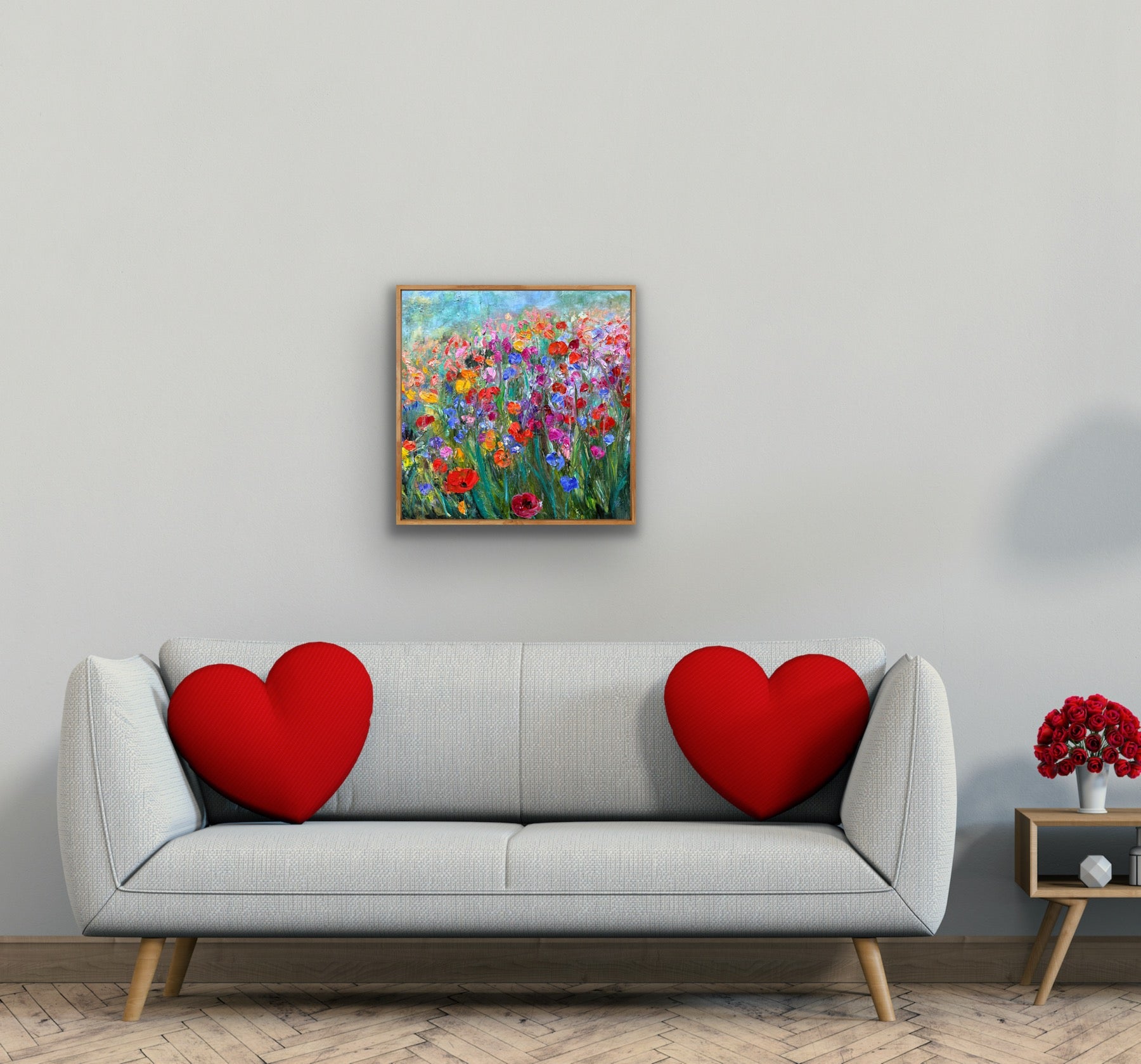 Gray sofa with red heart-shaped cushions, colorful floral painting on the wall, and small table with red flowers.