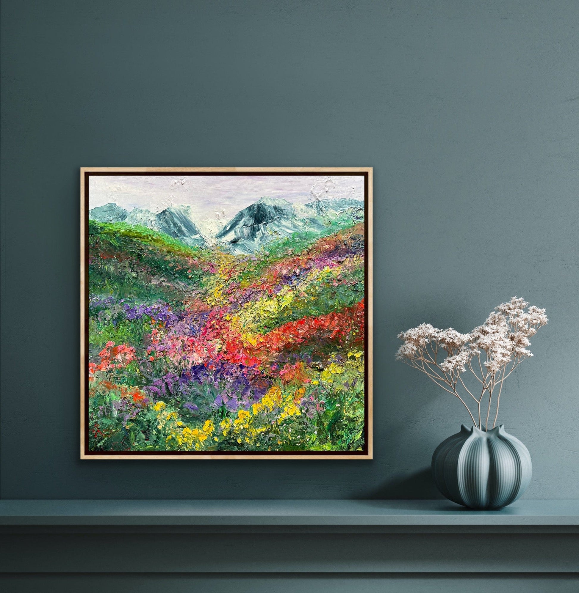 Happy Valley impressionist flower field painting by Maria-Victoria Checa in a natural wood float frame displayed on a deep teal wall above a console table, showing scale in a moody modern interior.