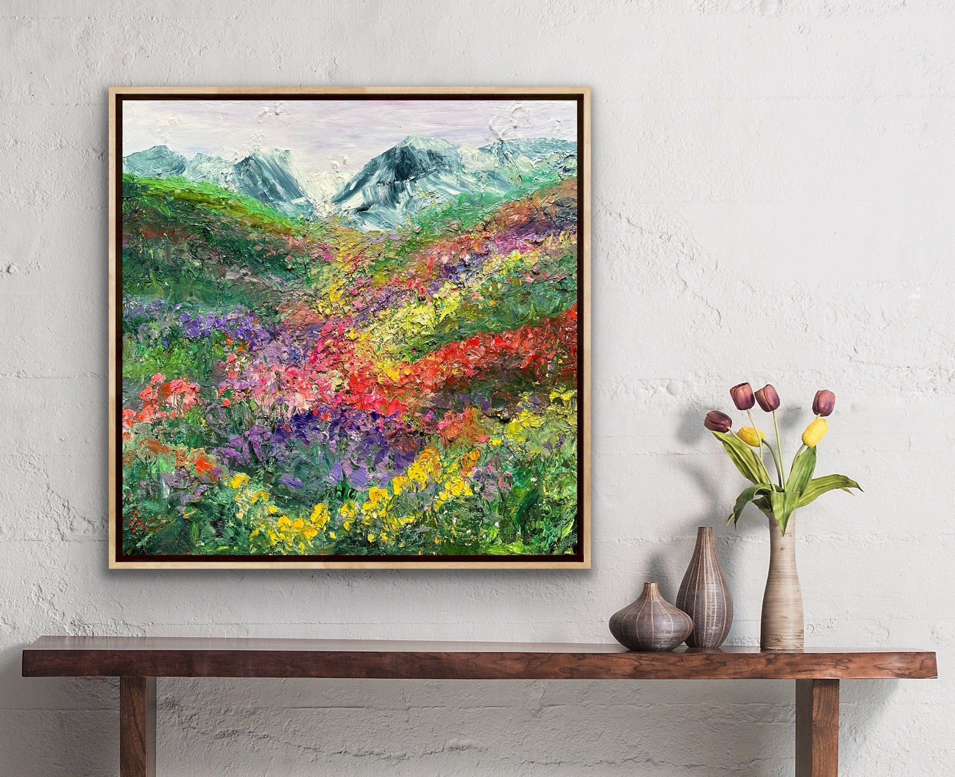 Happy Valley impressionist flower field painting by Maria-Victoria Checa in a natural wood float frame displayed on a white textured wall above a wooden console table in a warm bohemian room setting.