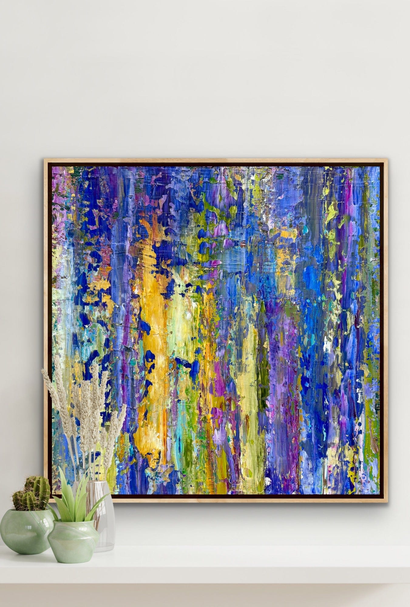 Lavender original abstract painting by Maria-Victoria Checa shown on a white wall above a shelf with green ceramic vases, highlighting textured blue, violet, and yellow acrylic layers.