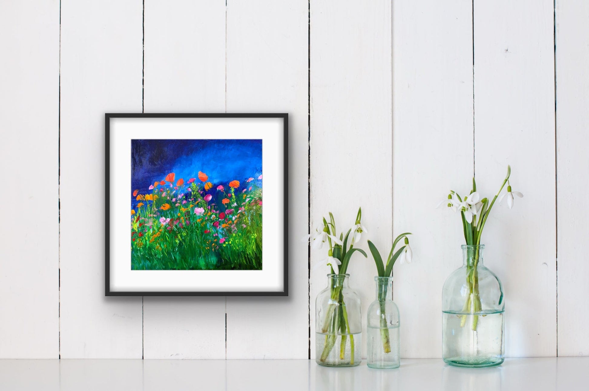 Midnight Dream framed paper print by Maria-Victoria Checa in a black frame with white mat, displayed on a white shiplap wall beside glass bud vases in a bright cottage interior