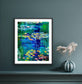 Framed paper print with mat of “Water Lily Pond” by Maria-Victoria Checa displayed on a blue wall above a console, showing vibrant water lilies and reflective blue water.