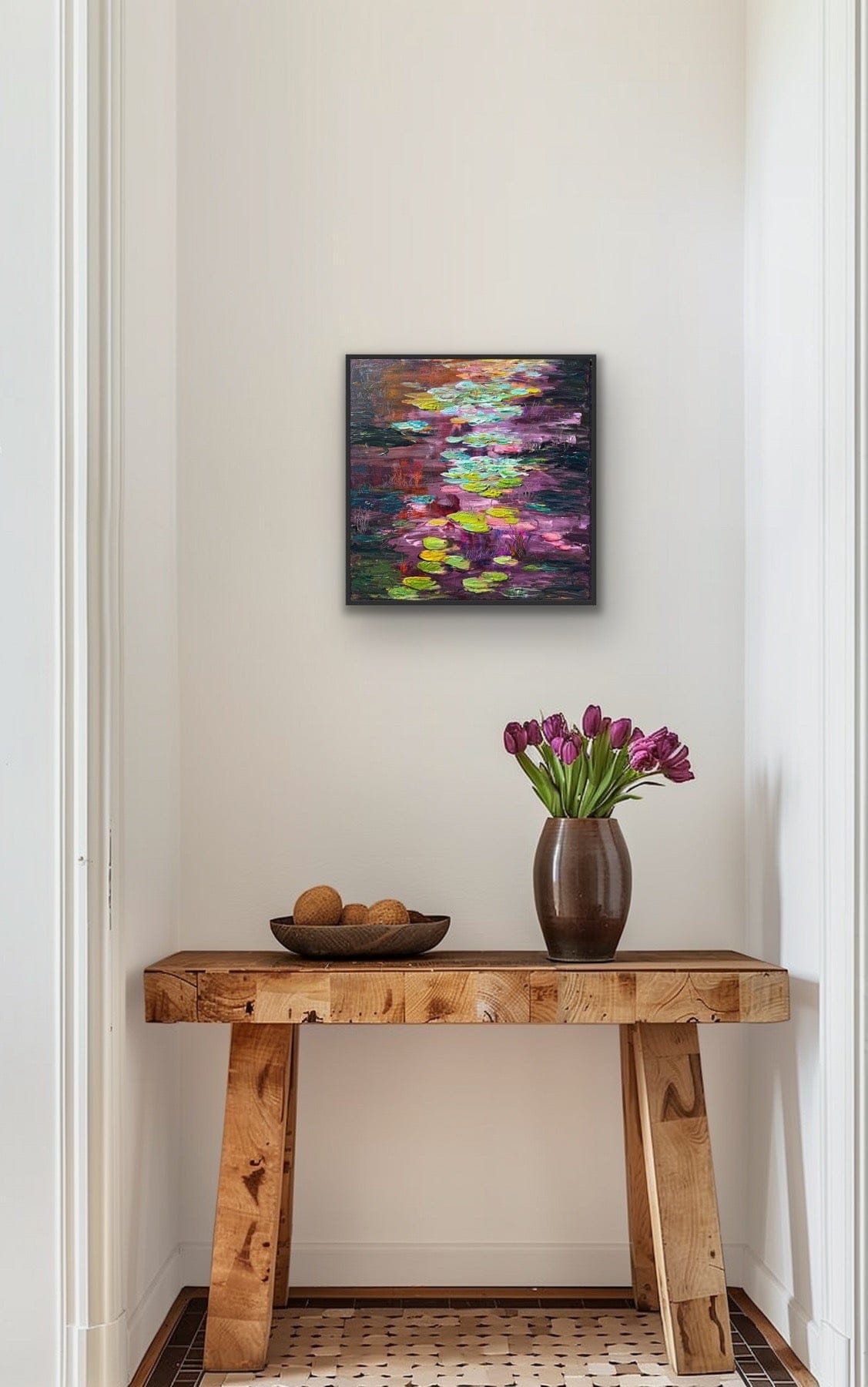 Framed impressionist landscape painting  by Maria-Victoria Checa shown above a table with vase of tulips and bowl of fruits.