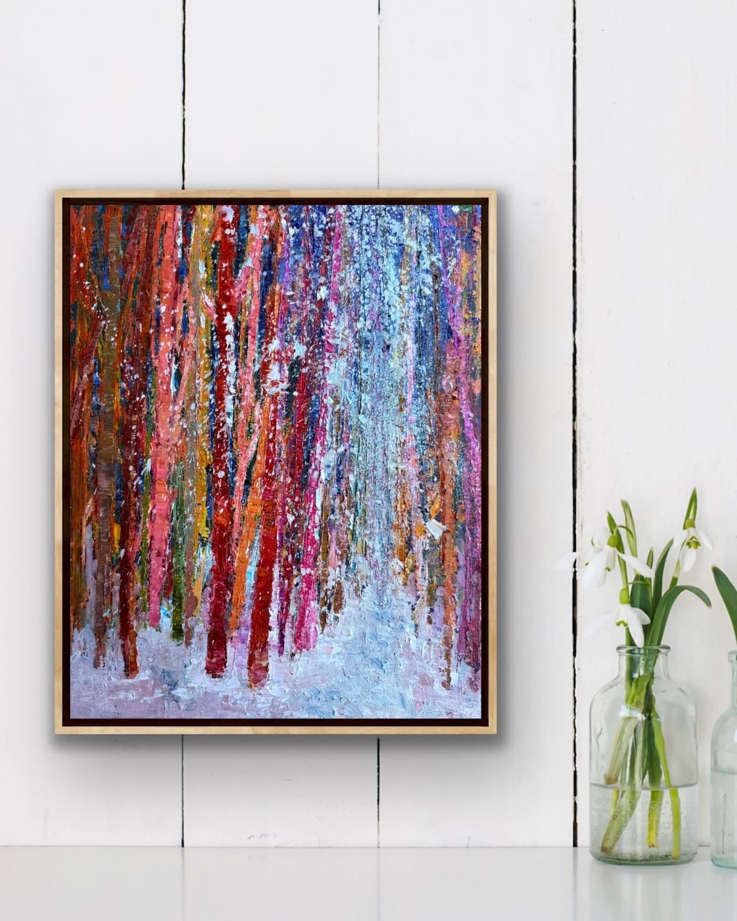 Framed Winter Land Path forest painting by Maria-Victoria Checa hanging on a white shiplap wall beside a vase of snowdrops