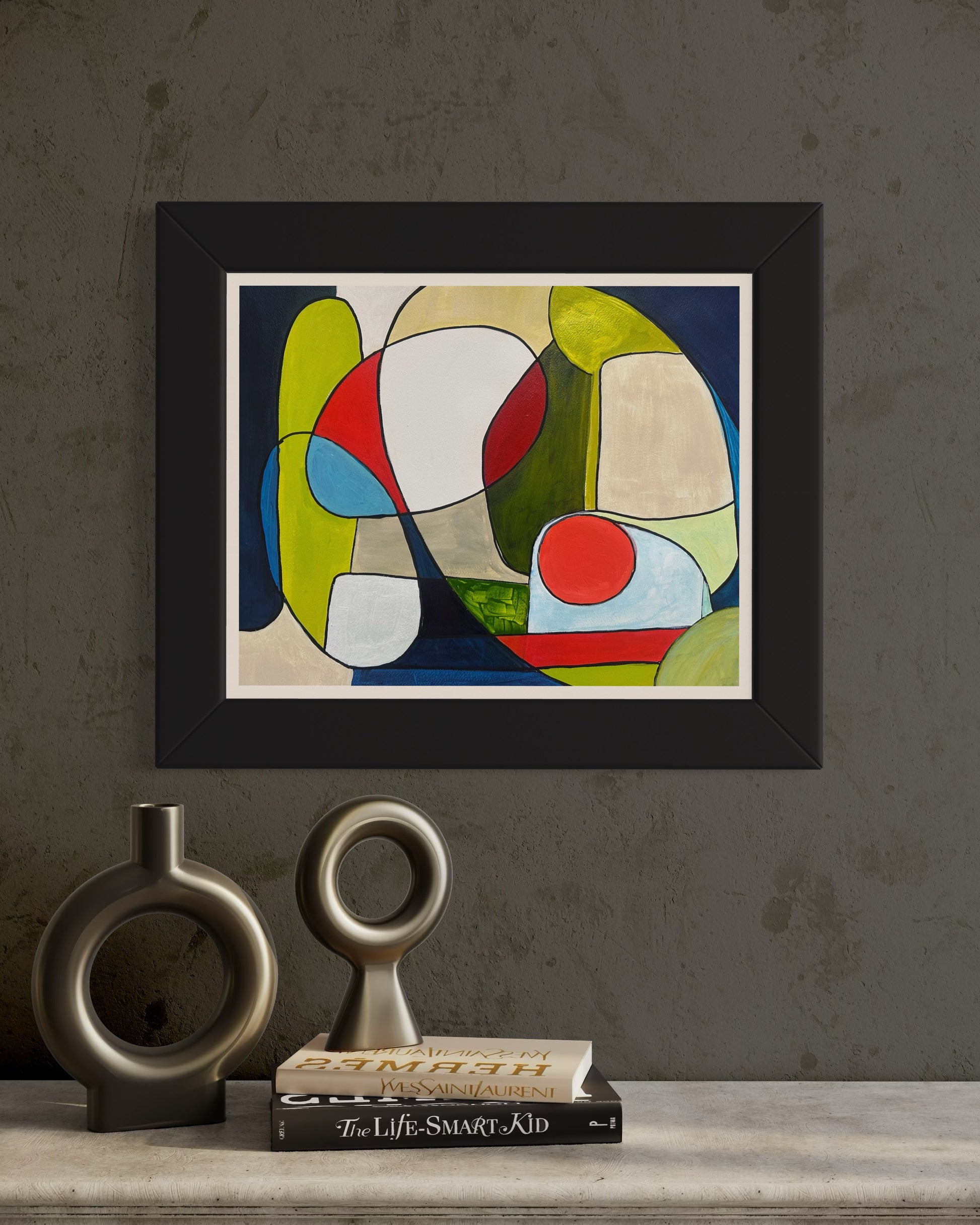 Framed abstract artwork ‘You and Me’ by Maria-Victoria Checa styled on a textured wall above books and modern circular sculptures.